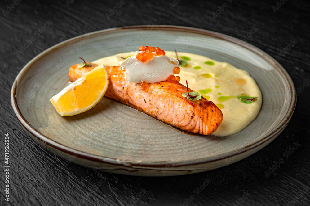 Salmon fillet with mascarpone, red caviar and tender puree in a ceramic plate on a dark textured background. Restaurant menu Isolated on black