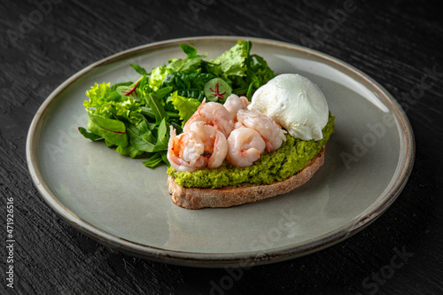 Bruschetta with cocktail shrimp, guaccamolle and poached egg in a ceramic plate on a dark textured background. Restaurant menu Isolated on black