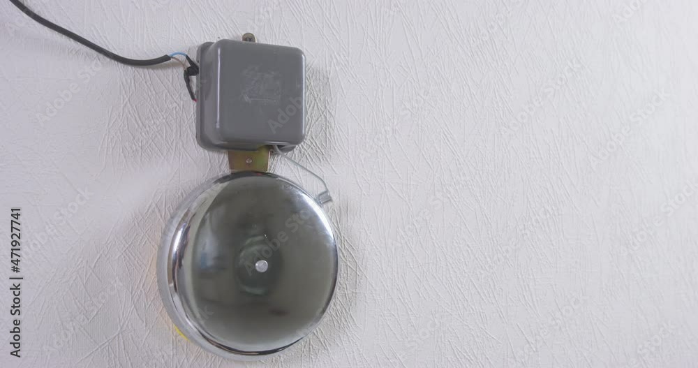 Steel school bell hanging on white plastered wall IN hall rings loudly announcing beginning or ending of lessons extreme closeup Steel school bell hanging on white plastered wall IN hall rings loudly announcing beginning or ending of lessons extreme closeup