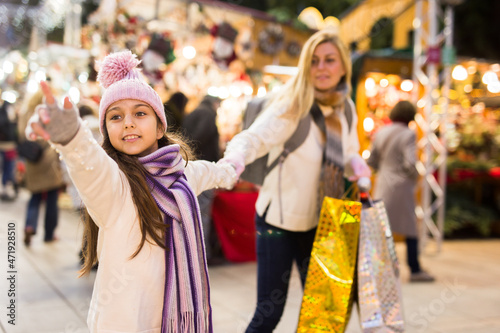 Young mother with her daughter shopping on outside Christmas market pointing to something