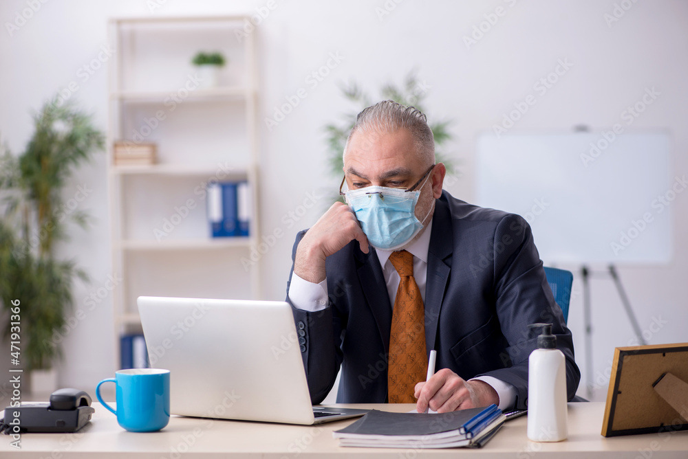 Old male employee working in the office during pandemic