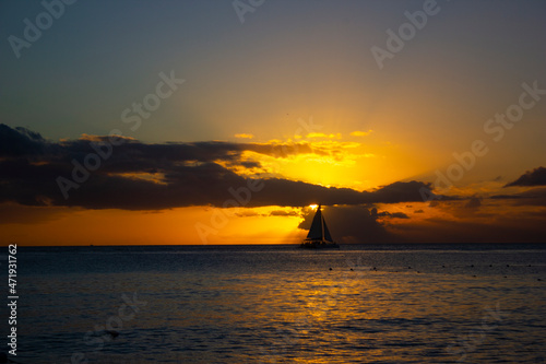 SUNSET ON THE BEACH WITH BOATS IN THE ORIZON AND ORANGE SUNLIGHT, WITH BLUE SKY AND SOME CLOUDS