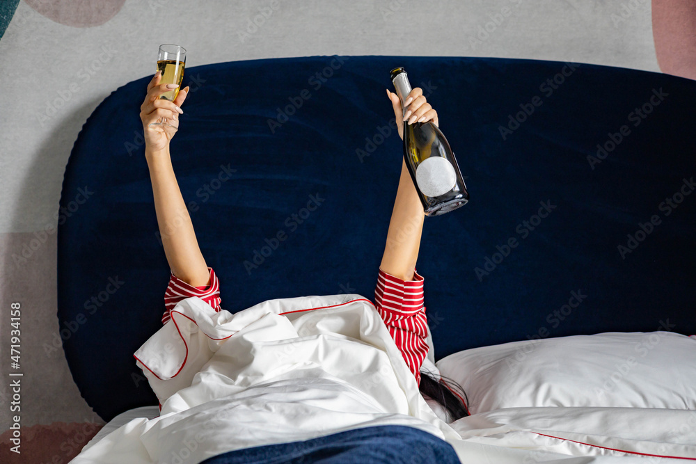 Happy young domestic woman in red pajamas drinking champagne wine