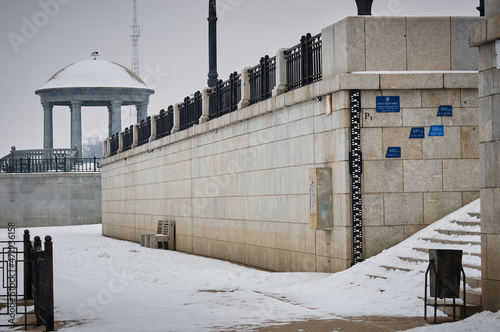 Inscription on Russian Hydrometeorological point on the Amur river embankment. Water level marks of the river in floods of different years. Snow on the stairs and rotunda in blur. Winter cityscape. photo