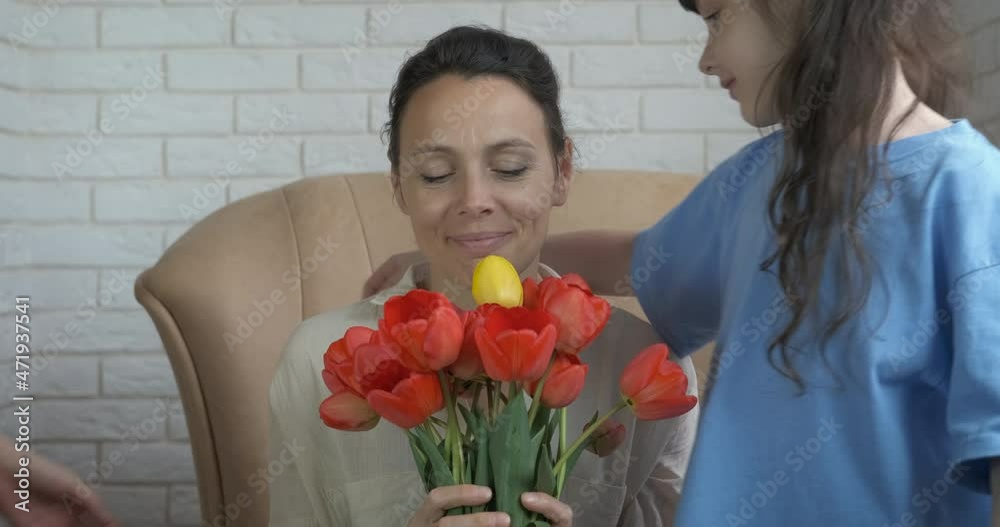 Family joy with flowers at home. Two little girls sit by their mother with flowers and hug her. Mother's Day. Family joy with flowers at home. Two little girls sit by their mother with flowers and hug her. Mother's Day.