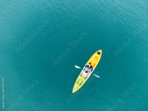 Unidentified man on sea Kayaker Aerial View during sunset. Caucasian Sportsman in the Yellow and Blue Kayak Paddling on the Scenic sea Along the Shore.