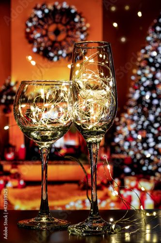 A transparent wine glass and a champagne glass filled with bright light bulbs create a festive mood and a desire to celebrate. Beautiful, transparent glasses shine, Merry Christmas and Happy New Year.