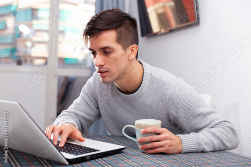 Portrait of cheerful male who is working with laptop at the table at the home photo