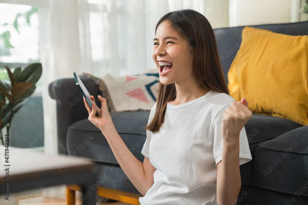 Excited Young Asian woman playing an online game on a smartphone with fists clenched celebrating victory expressing success Excited Young Asian woman playing an online game on a smartphone with fists clenched celebrating victory expressing success
