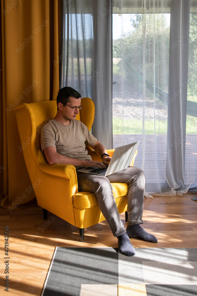Comfortable home office. A man is sitting and working in a big yellow armchair
