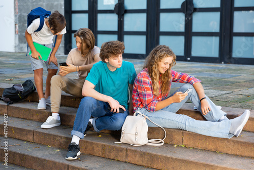 Group of teenagers sitting on stairs in school campus and using smartphones.