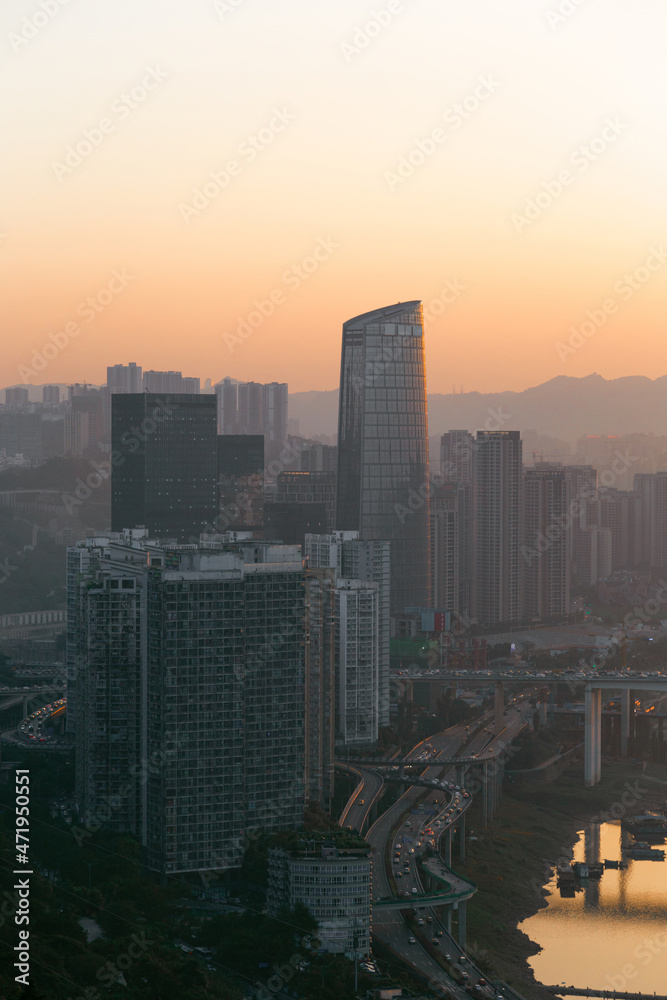 Fototapeta premium At sunset, the river banks flowing with vehicles, the sun's afterglow sprinkled on the skyscrapers, the river; in the distance is the sunset , the silhouette of the mountains, this is Chongqing, China