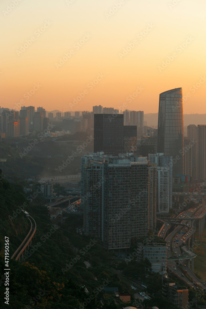 A city view at sunset, here in Chongqing, China. Next to the skyscrapers is the city transportation track, and in the distance is the silhouette of the sun setting over the mountains