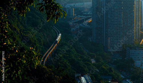 Urban rail transit runs between the trees on the slopes of Goose Ridge Park in Chongqing, China. Sunset spills over it