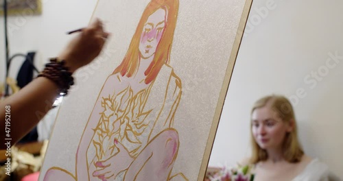 Unrecognizable artist making art portrait of Caucasian girl sitting behind on sofa indoors studio room. Female hands holding brush tool painting picture of young woman natural light. Master class 