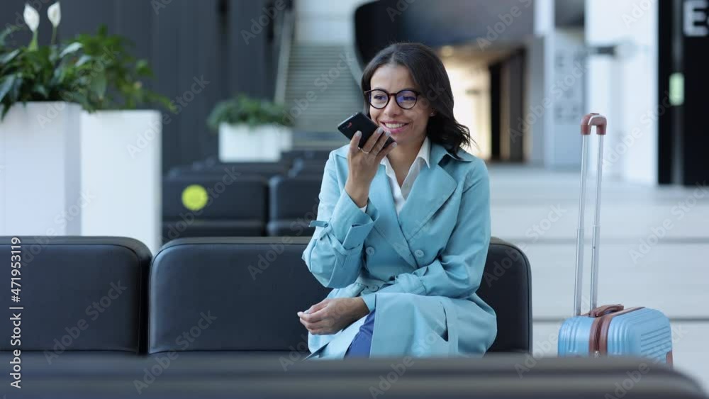Successful businesswoman having online talk with smartphone in hand, sitting in airport room spbi. Young African American woman holds phone and looks with smile, discusses business and waits for Successful businesswoman having online talk with smartphone in hand, sitting in airport room spbi. Young African American woman holds phone and looks with smile, discusses business and waits for