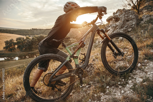 Fototapeta Naklejka Na Ścianę i Meble -  Young male cyclist rolling bike on grassy mountain slope in sundown