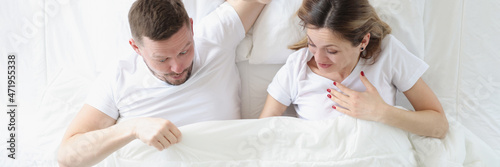 Joyful man and woman looking under blanket while lying in bed