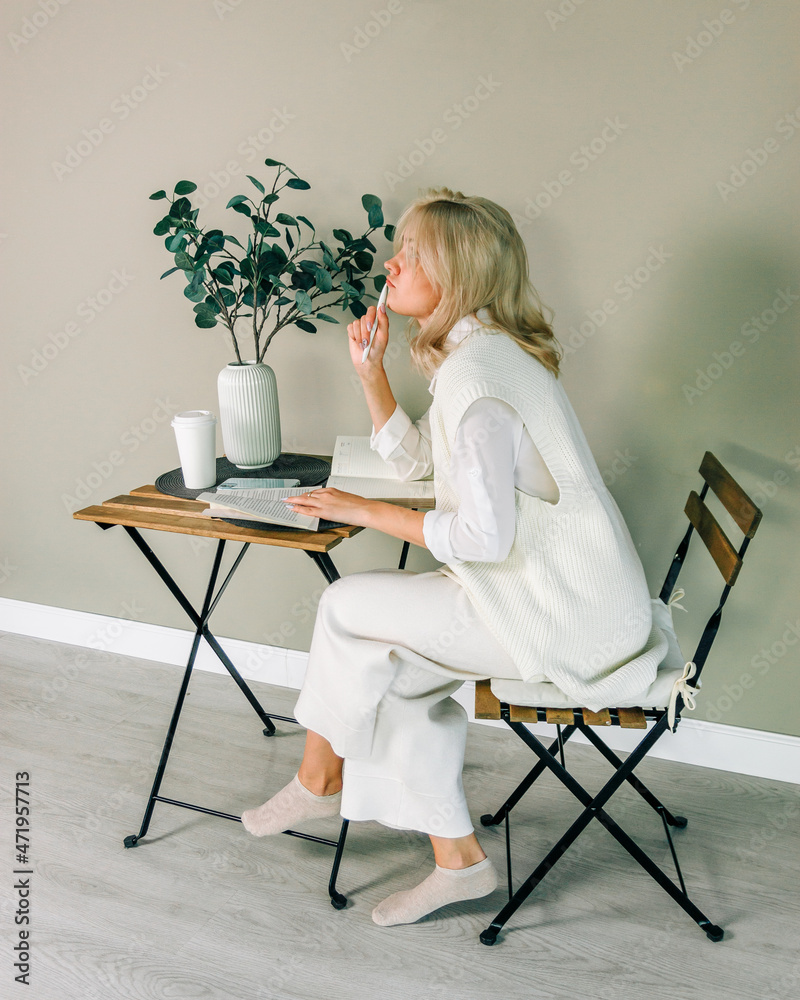Side view of a dreaming young girl at a coffee table with a book and a phone Side view of a dreaming young girl at a coffee table with a book and a phone