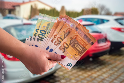 hands of a young woman holding a euro banknote on a background of cars