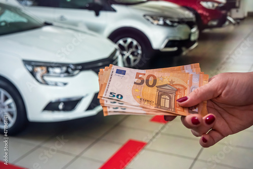 beautiful hand willingly holds new euro banknotes on a background of beautiful new cars. photo
