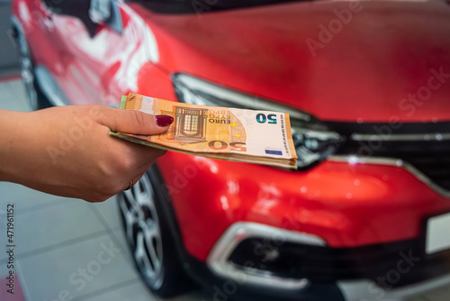 beautiful young hands holding a large amount of euro banknotes near cars in the parking lot. © RomanR