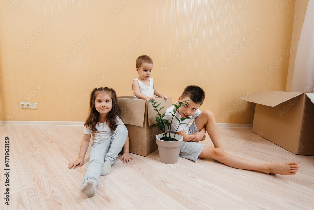 Little kids brothers and sister are sitting together on the floor against the background of cardboard boxes, rejoicing at the housewarming in a new apartment. Loan, the concept of home improvement. Little kids brothers and sister are sitting together on the floor against the background of cardboard boxes, rejoicing at the housewarming in a new apartment. Loan, the concept of home improvement.