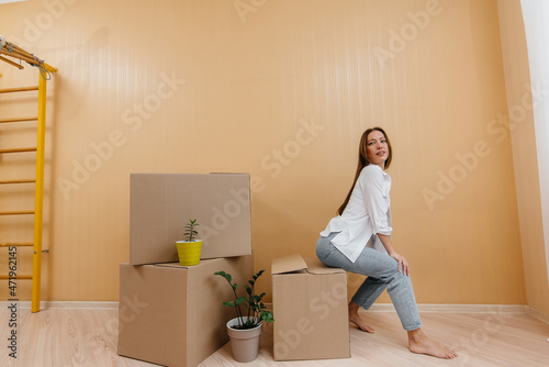 A young woman is sitting on a cardboard box and is happy about moving to a new home. Mortgage loan, the concept of home improvement. Housewarming. © Andrii