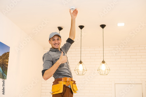 Young electrician installing smoke detector on ceiling