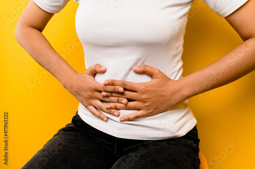 Asian woman has a stomachache She wakes up in the middle of the night while she sleeps. On a yellow background with professional photography lighting.