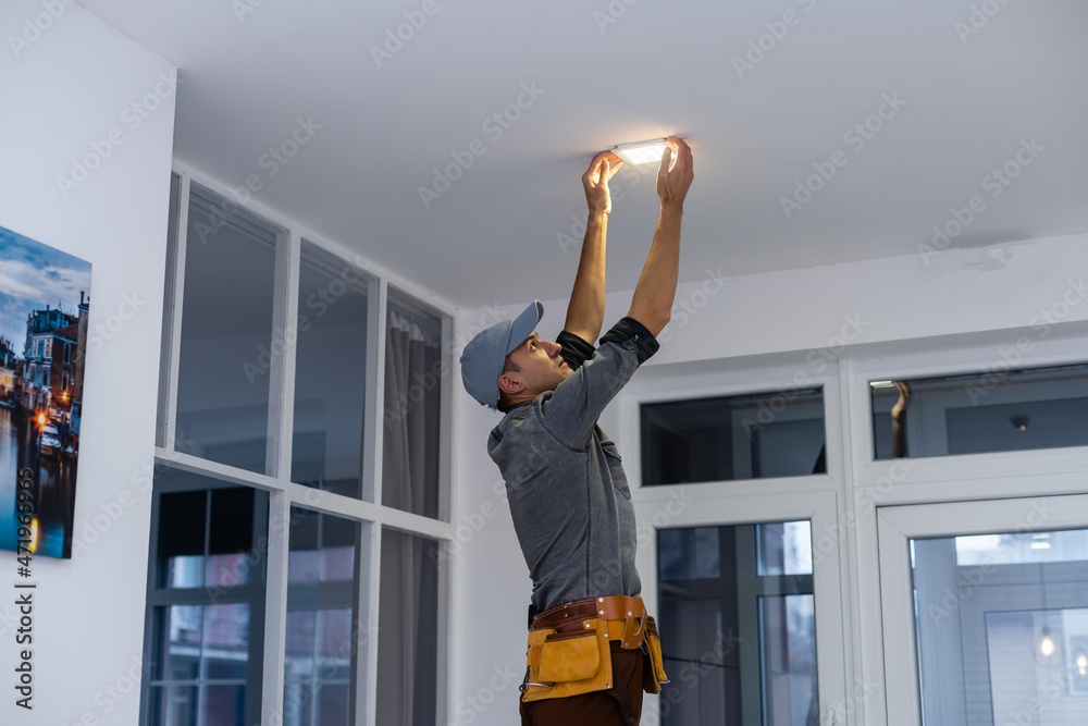 An electrician is installing spotlights on the ceiling - obrazy, fototapety, plakaty 