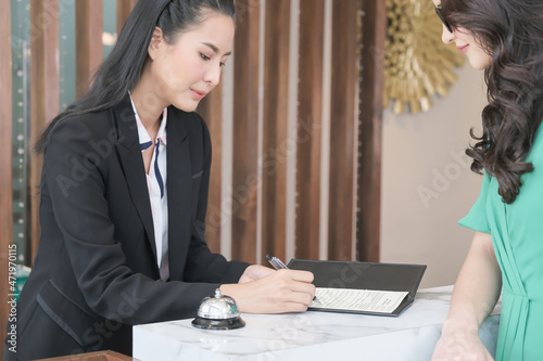 Asia girl receptionist and Caucasian woman traveler checking or checkout in hotel