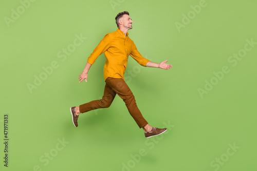 Full size profile side photo of mature man runner jump look empty space greeting isolated over green color background