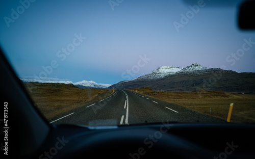 Travel  driving car on a beautiful scenic road in Iceland during sunrise in the background mountains are covered by snow