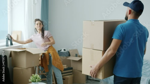 Male mover wearing uniform is bringing cardboard boxes to woman's new apartment helping with relocation. Delivery service and accommodation concept. photo