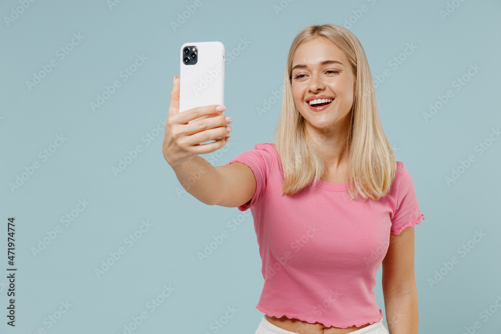 Full body young blonde woman 20s wearing casual pink t-shirt sit in bag chair doing selfie shot on mobile cell phone post photo on social network isolated on plain pastel light blue background studio. Full body young blonde woman 20s wearing casual pink t-shirt sit in bag chair doing selfie shot on mobile cell phone post photo on social network isolated on plain pastel light blue background studio.