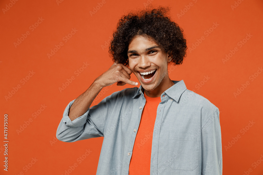 Young fun student black man 50s wearing blue shirt t-shirt look camera doing phone gesture like says call me back isolated on plain orange color background studio portrait. People lifestyle concept. Young fun student black man 50s wearing blue shirt t-shirt look camera doing phone gesture like says call me back isolated on plain orange color background studio portrait. People lifestyle concept.