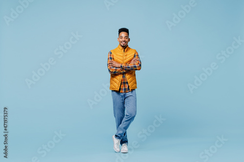 Full size body length smiling fascinating young black man 20s years old wears yellow waistcoat shirt looking camera hold hands crossed isolated on plain pastel light blue background studio portrait.