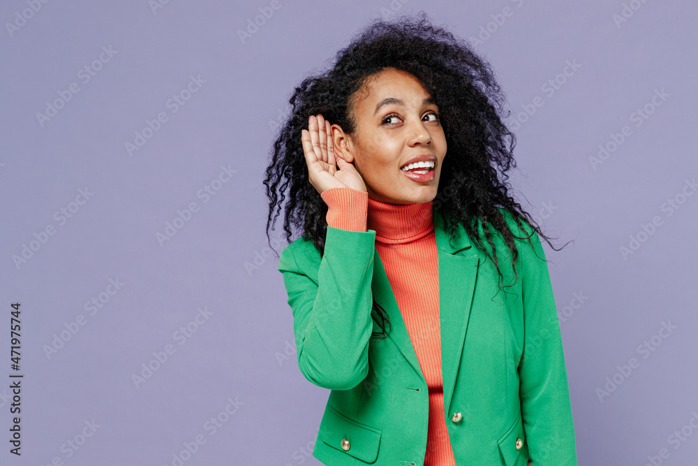 Curious nosy young black curly woman 20s wears green shirt try to hear you overhear listen intently isolated on plain pastel light violet background studio portrait. People emotions lifestyle concept. Curious nosy young black curly woman 20s wears green shirt try to hear you overhear listen intently isolated on plain pastel light violet background studio portrait. People emotions lifestyle concept.