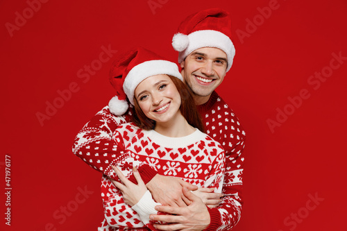 Young smiling lovely couple friends two man woman 20s in sweater hat hugging cuddle look camera isolated on plain red background studio Happy New Year 2022 celebration merry ho x-mas holiday concept.