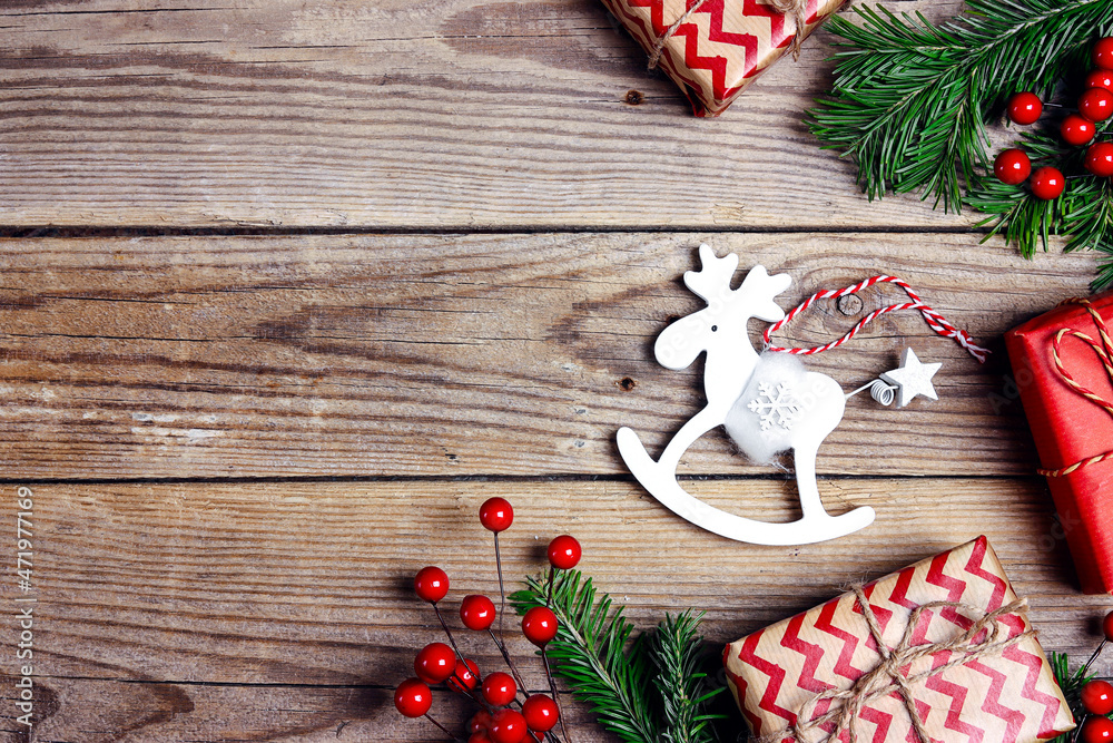 Christmas background with toy elk, gifts, fir branches and red berries on a wooden table.