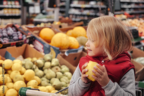 Little girl sitting in shopping cart in food fruit store or supermarket