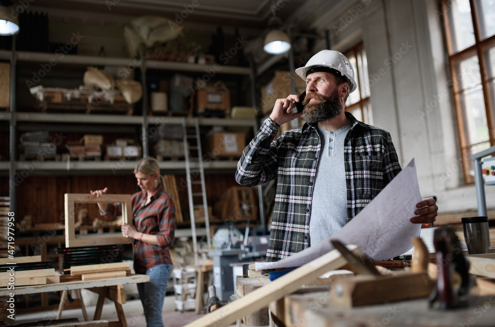 Low angle view of mature male carpenter looking at blueprints plans in carpentery workshop.