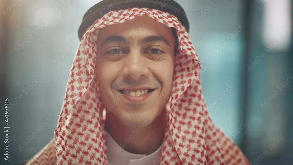 Portrait of Young Successful Arab Businessman in Traditional Outfit Gently Smiling, Wearing White Kandura and Black Agal Keeping a Ghutra in Place. Saudi, Emirati, Arab Businessman Concept. Portrait of Young Successful Arab Businessman in Traditional Outfit Gently Smiling, Wearing White Kandura and Black Agal Keeping a Ghutra in Place. Saudi, Emirati, Arab Businessman Concept.