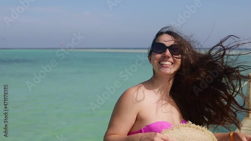 smiling young woman in sunglasses and straw hat with hair blowing in the wind