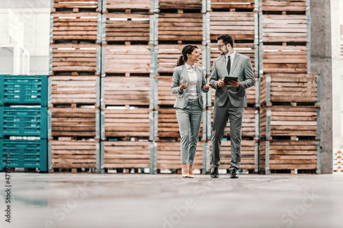 Business talk and walk in the warehouse. Man and a woman in a business suit stand in a warehouse and check the situation. Man holds a tablet in his hand and points a finger at the woman at something