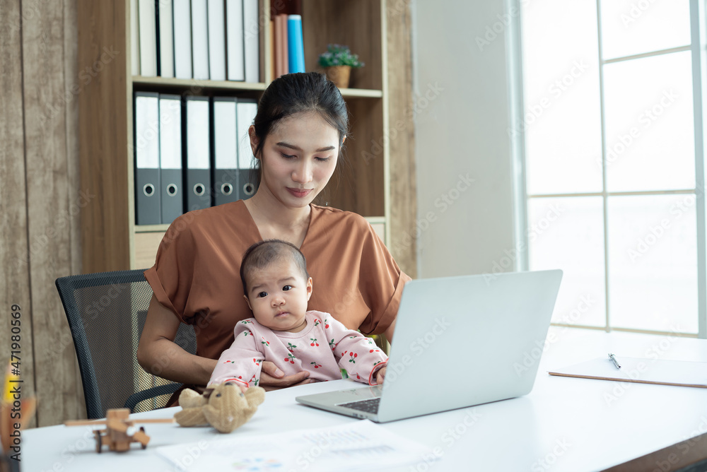 Busy woman trying to work while babysitting newborn baby daughte. Young beautiful Asian mother holding little baby on lap while another hand typing. Working women with multitasking. Busy woman trying to work while babysitting newborn baby daughte. Young beautiful Asian mother holding little baby on lap while another hand typing. Working women with multitasking.