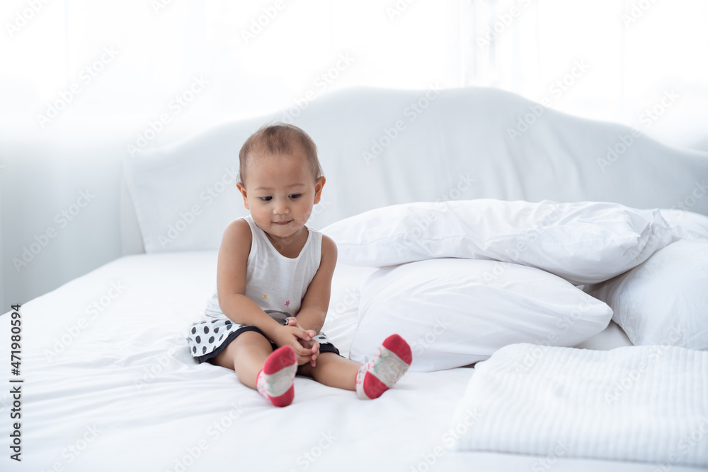 little lovely Asian toddler sitting on white bed, nursery place, baby playing alone little lovely Asian toddler sitting on white bed, nursery place, baby playing alone