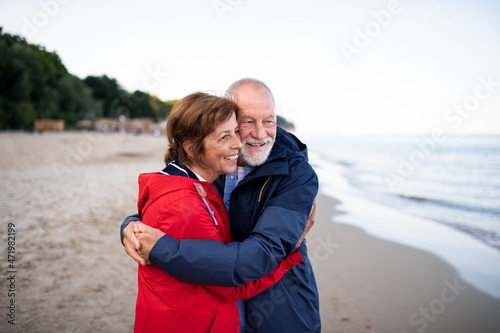 Happy senior couple in love embracing when walking on sandy beach in autumn.
