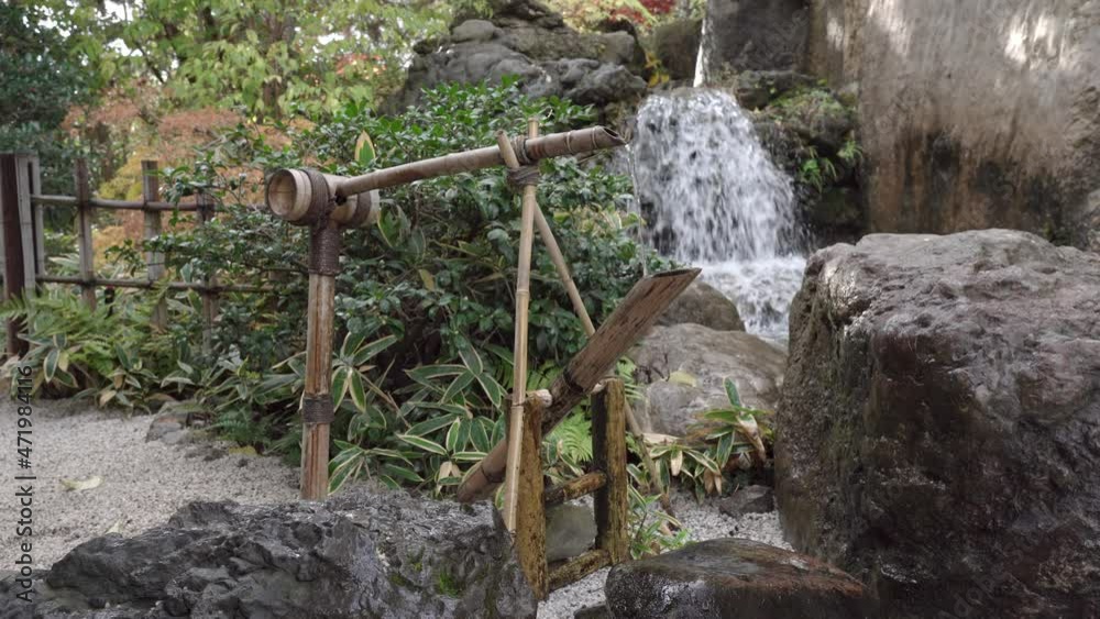 Sozu (Shishi-odoshi, deer repeller) in a Japanese garden. A device used in Japanese gardens. A vessel from a bamboo trunk, when filled with water, overturns and makes a sound, water is poured out Sozu (Shishi-odoshi, deer repeller) in a Japanese garden. A device used in Japanese gardens. A vessel from a bamboo trunk, when filled with water, overturns and makes a sound, water is poured out